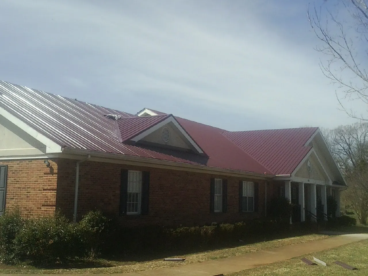 Red metal roof with gabled entries on a long brick building, from a Hail Damage Roof Repair job in Greenbush