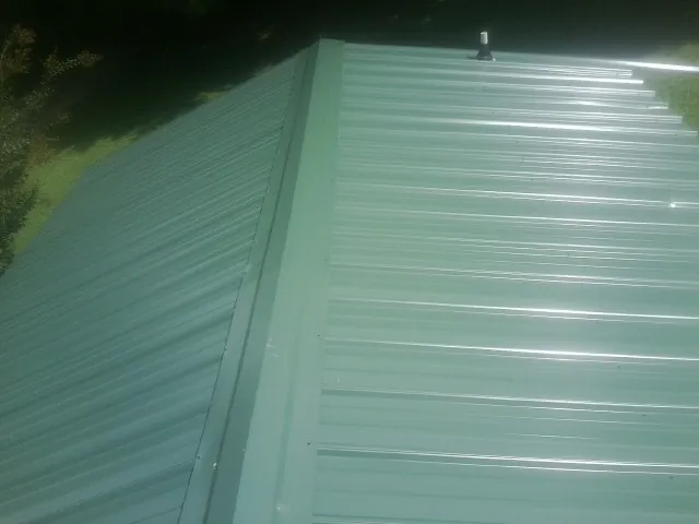 New green metal panels meeting at the ridge of a roof — Flat Roof Repair work by our crew in Greenbush