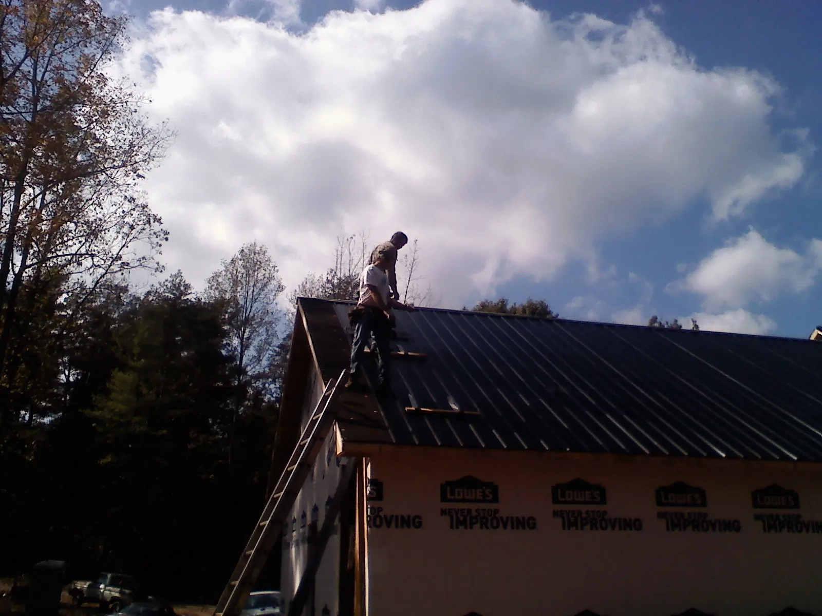 Roofer fastening dark metal panels high against a cloudy sky, from a Roof Inspection job in Greenbush