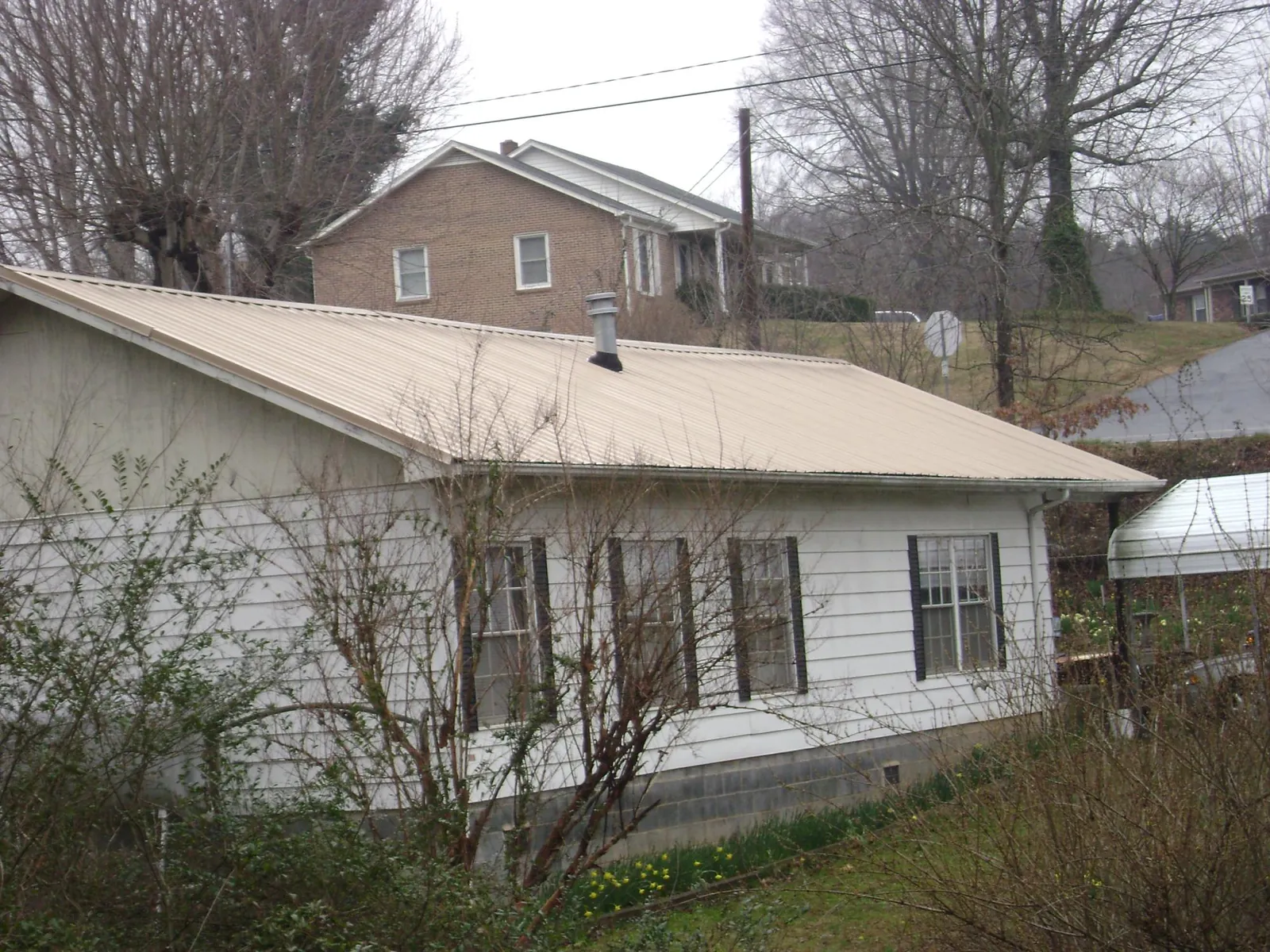 Tan metal roof on a white sided house set into a hillside — Commercial Roofing by Roofing Brothers in Greenbush