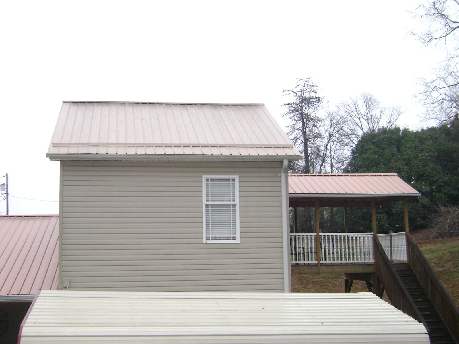 Tan metal roofs on a two story addition and attached porch, from a Roof Replacement job in Greenbush